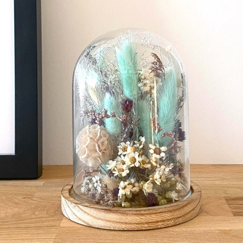 Composition de fleurs sechees dans les couleurs blanc bleu et violet delicatement arrangees sous un globe en verre