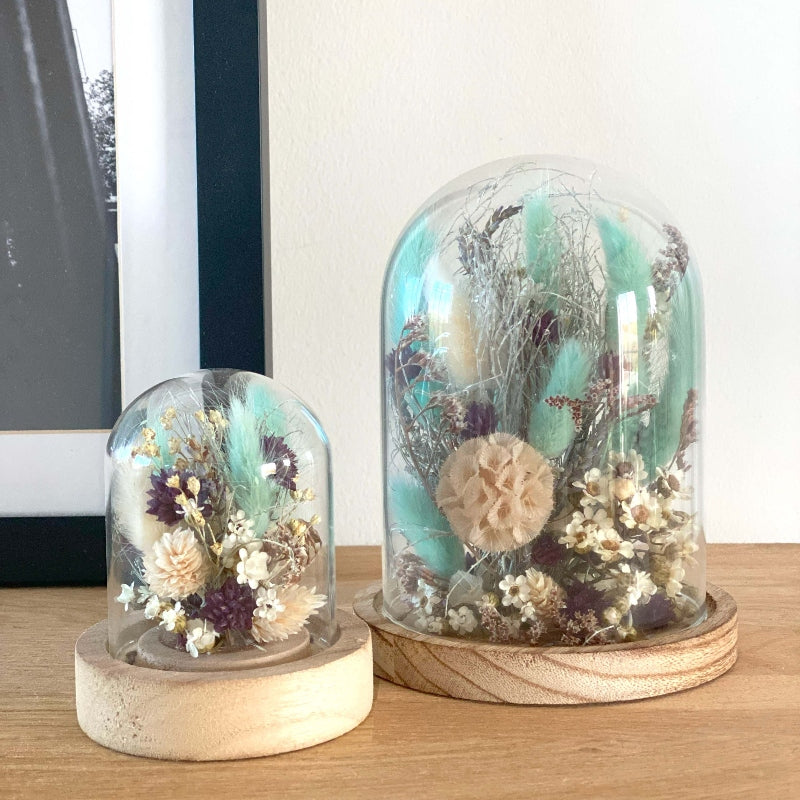 Composition de fleurs sechees dans les couleurs blanc bleu et violet delicatement arrangees sous un globe en verre