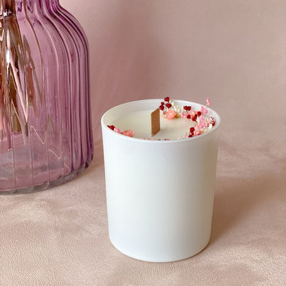 bougie en cire naturelle, décorée de petites fleurs sechees roses et blanches dans un pot blanc mat avec meche en bois. 