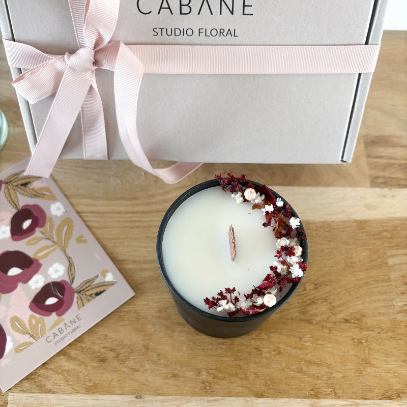 bougie fleurie scarlet 100% naturelle décorée de petites fleurs séchées dans les tons grenat, rose poudré et blanc et coulée dans un pot en verre noir mat très élégant.