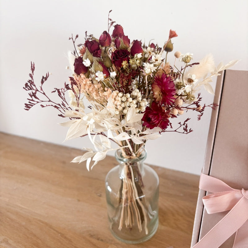 bouquet de petites roses rouges séchées et de fleurs séchées dans les tons rose poudré et blanc dans un vase en verre