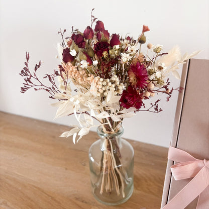 bouquet de petites roses rouges séchées et de fleurs séchées dans les tons rose poudré et blanc dans un vase en verre